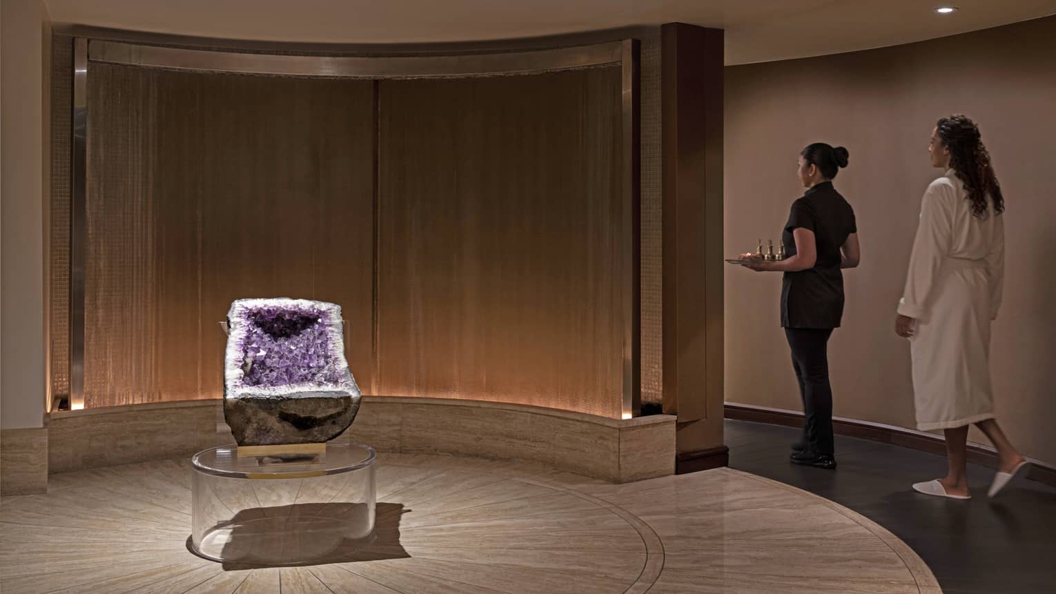 A spa team member walking with a woman in a spa robe.