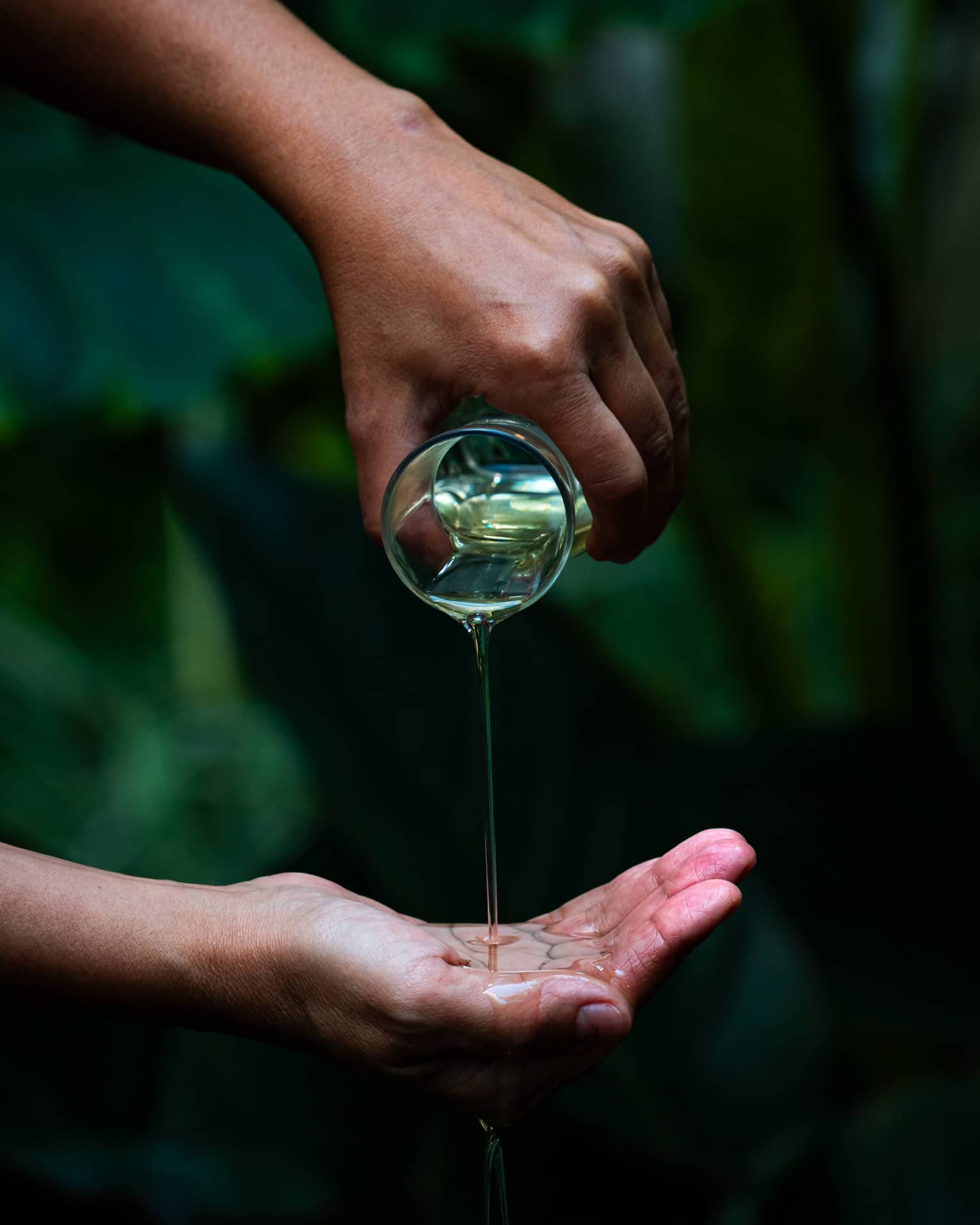 A person pours oil into cupped hand in garden setting