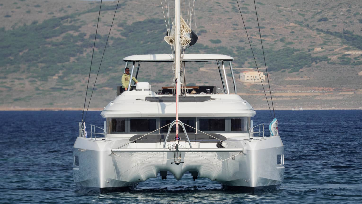 Stern view of luxury sailboat in blue water with captain at helm