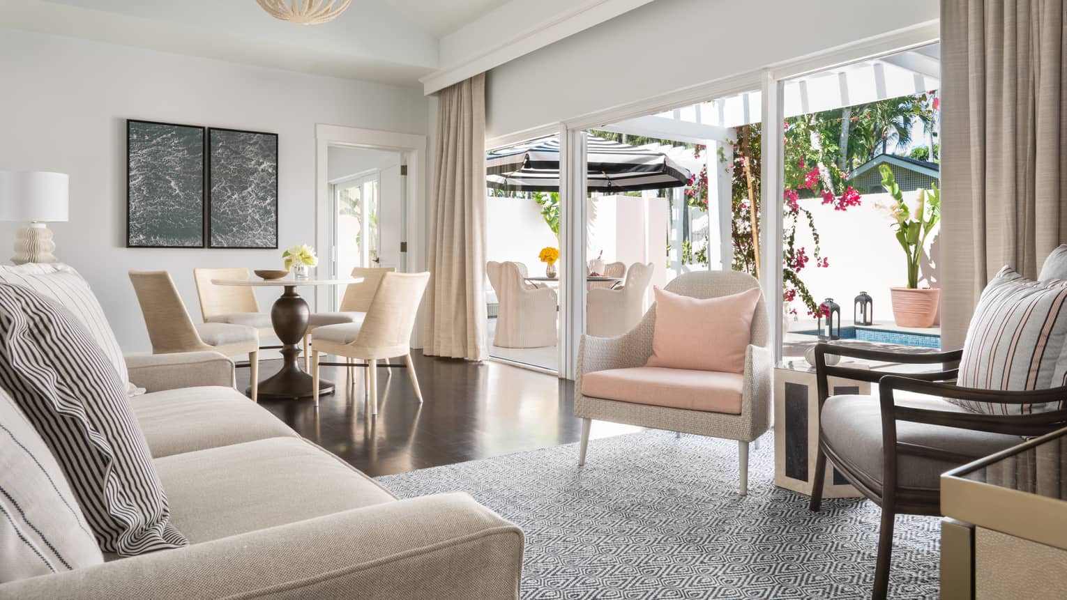 Plunge pool living room with neutral tones, featuring a sofa, dining table and sliding doors opening to an outdoor patio with seating and vibrant flowers