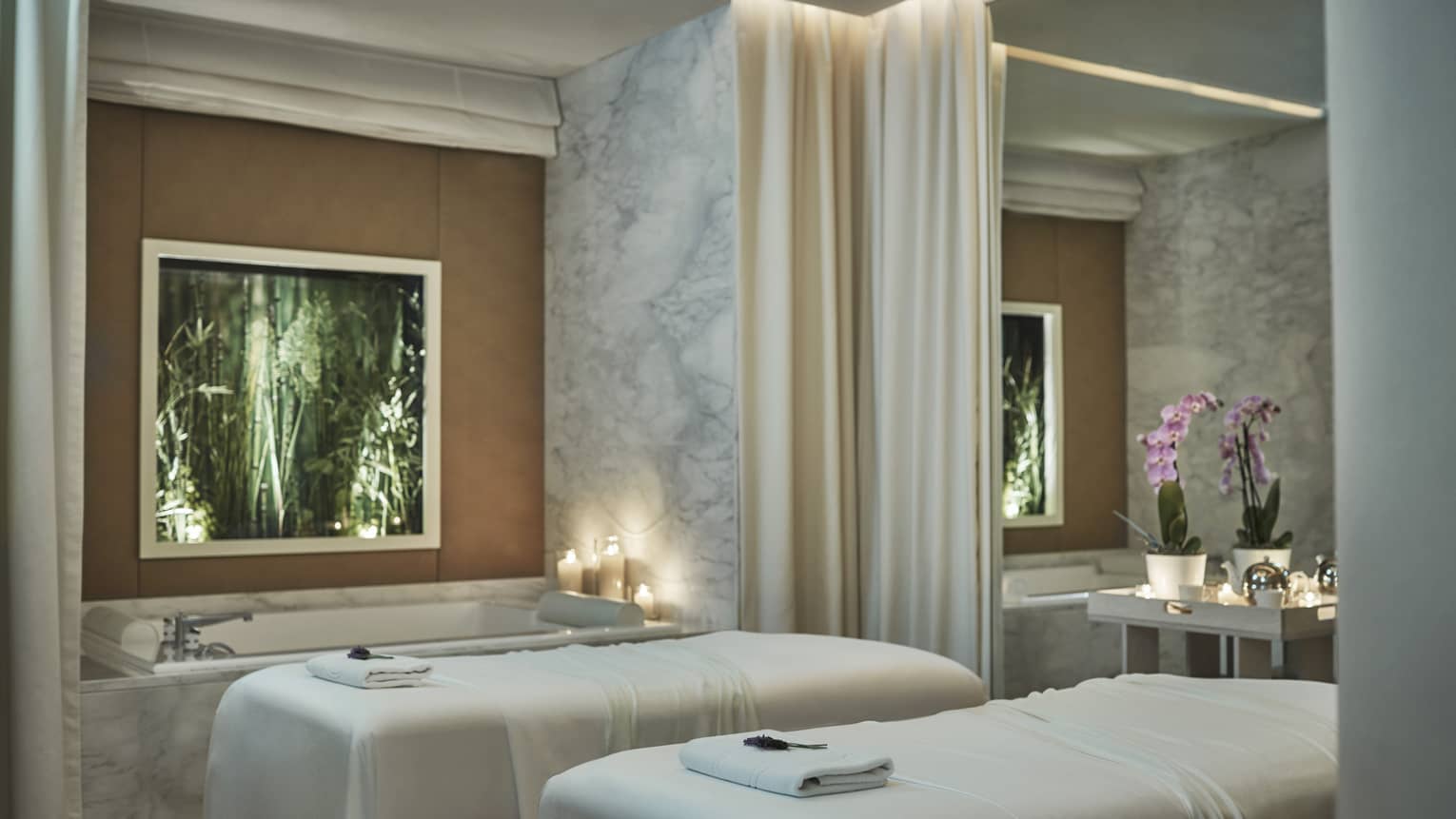 Spa couples massage beds with white sheets by candlelit tub