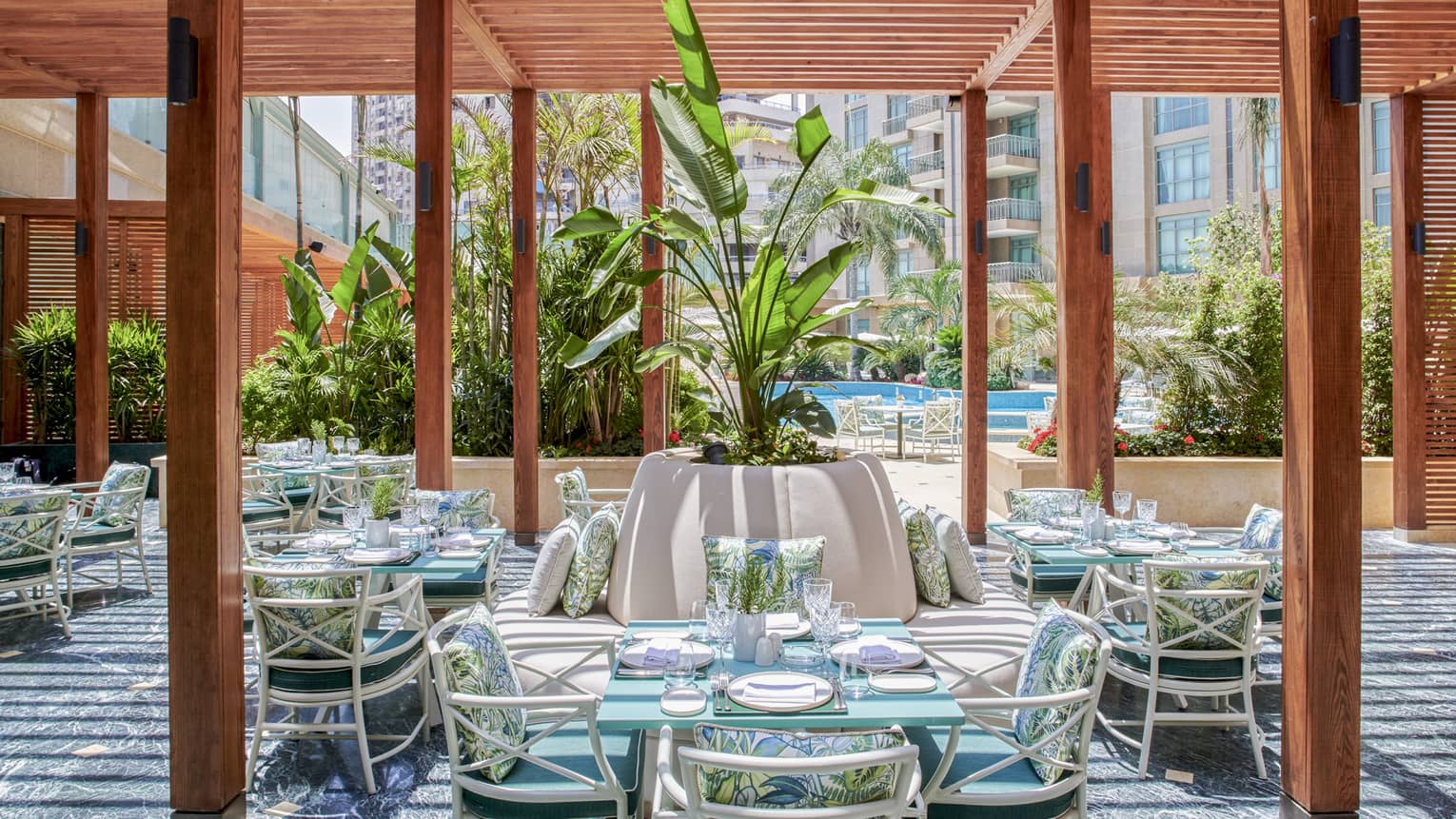 Byblos restaurant outdoor dining space with wooden columns, rattan chairs and square tables, large potted plant in middle