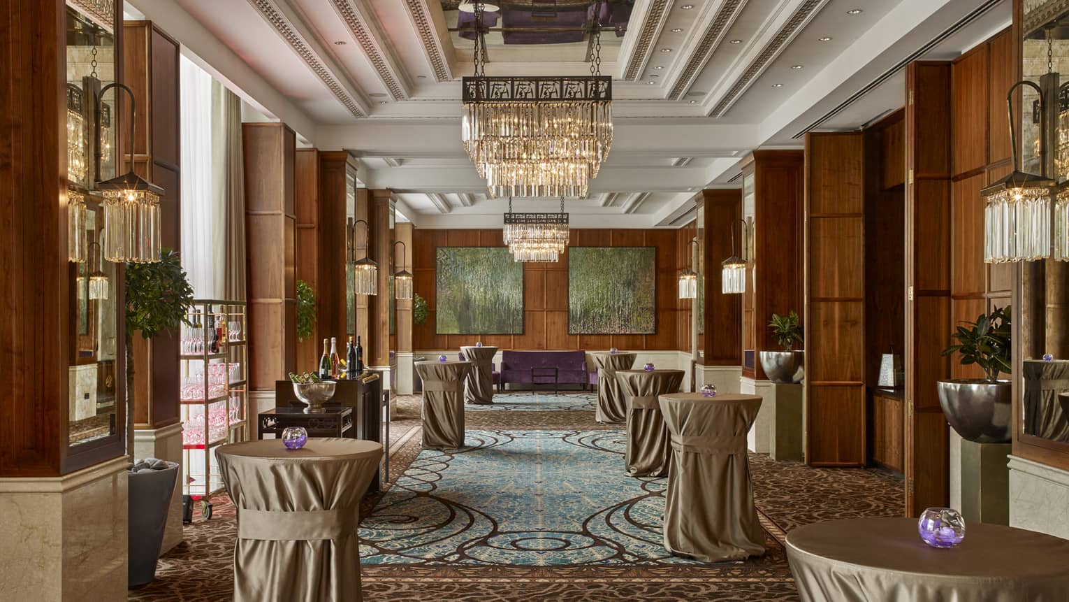 Room with large chandelier, drinks tables covered in tablecloths, bar with drinks
