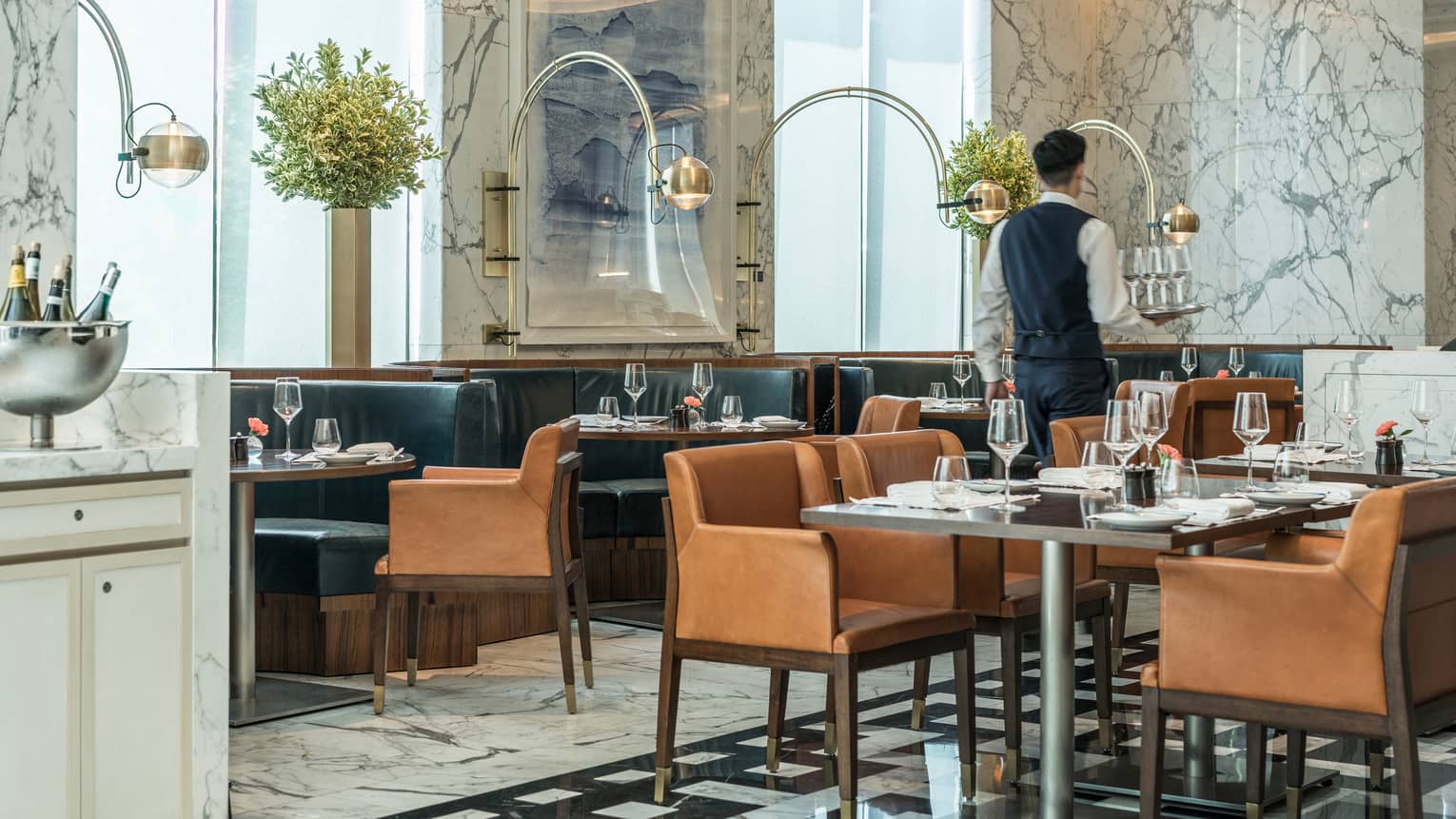 Server carries tray of glasses past lounge tables, chairs in Boccalino dining room
