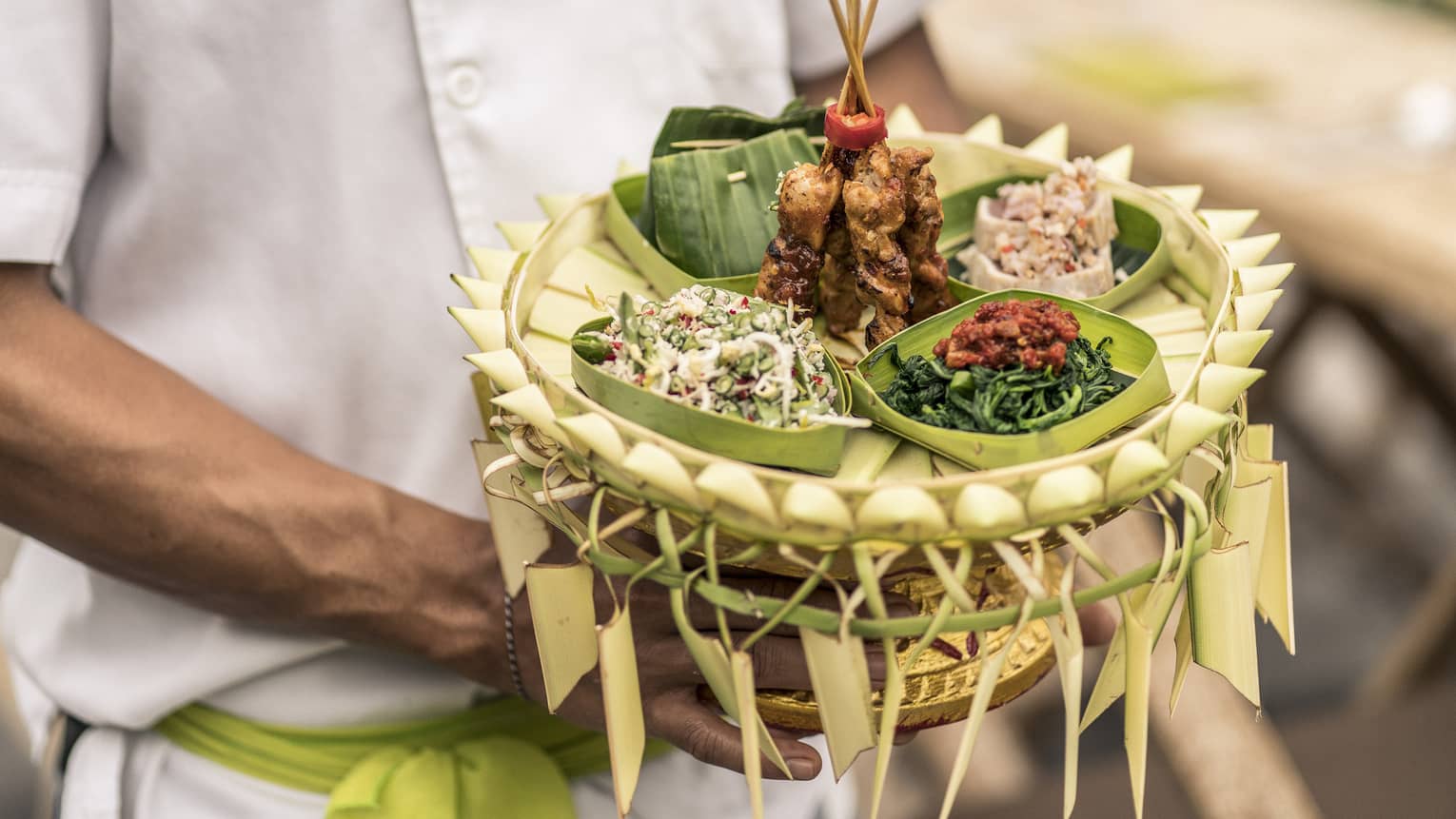 Close-up of a tray of food, including skewered meat, steamed vegetabes, chilis and fish served in banana leaves.