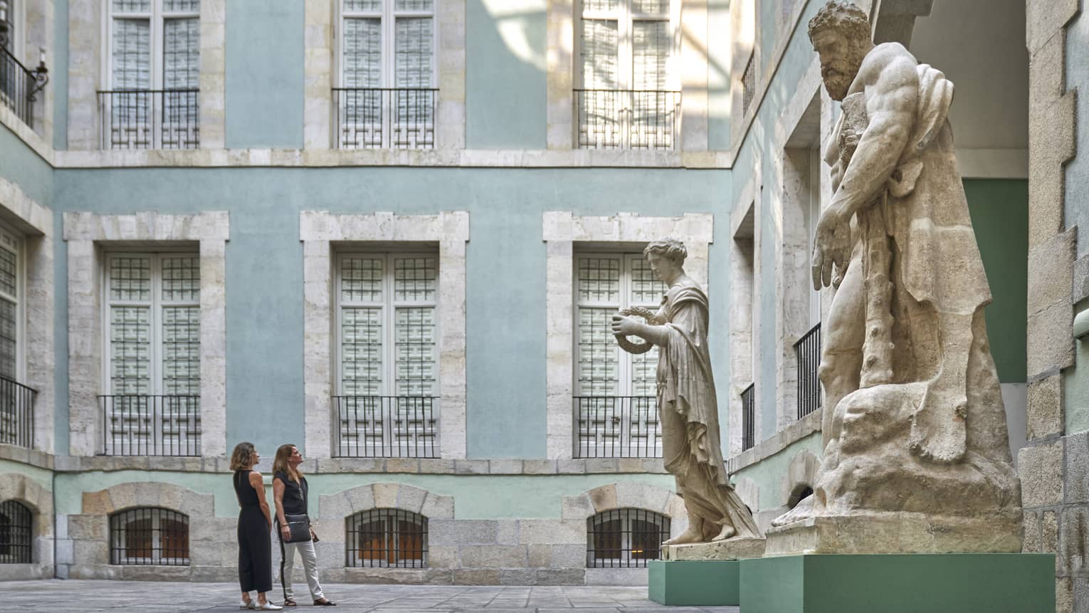 Two women observe large sculptures in a courtyard surrounded by light blue building