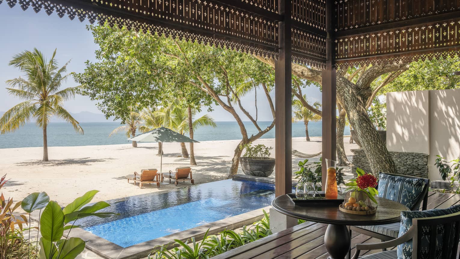 View of pool, beach and sea from covered terrace lounge