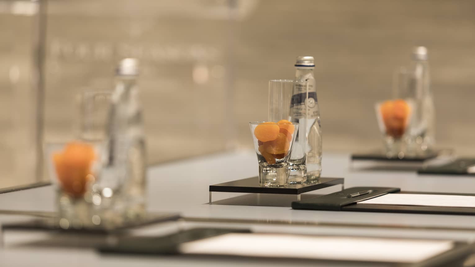 Close-up of meeting table place setting with agenda, dried apricots in glass, bottle of sparkling water