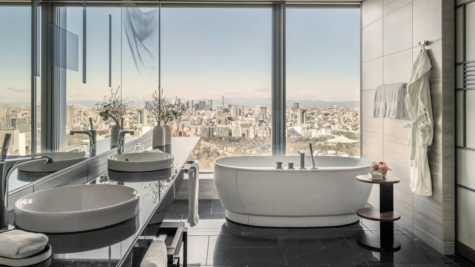 Large hotel suite bathroom with wall of window overlooking city, and a free-standing tub