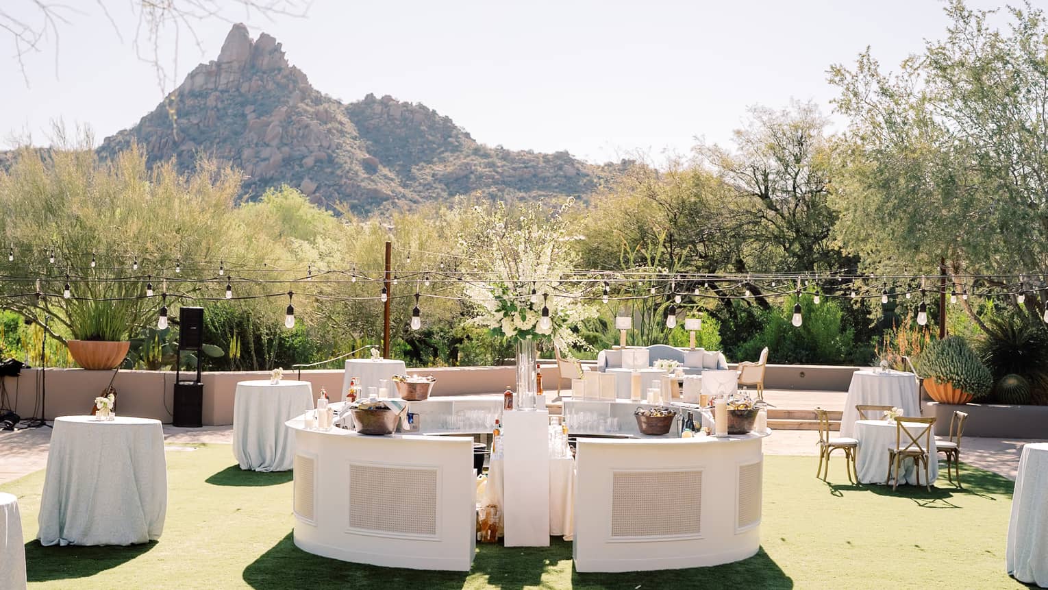 Outdoor wedding reception tables with string lights above and a mountain view in the background
