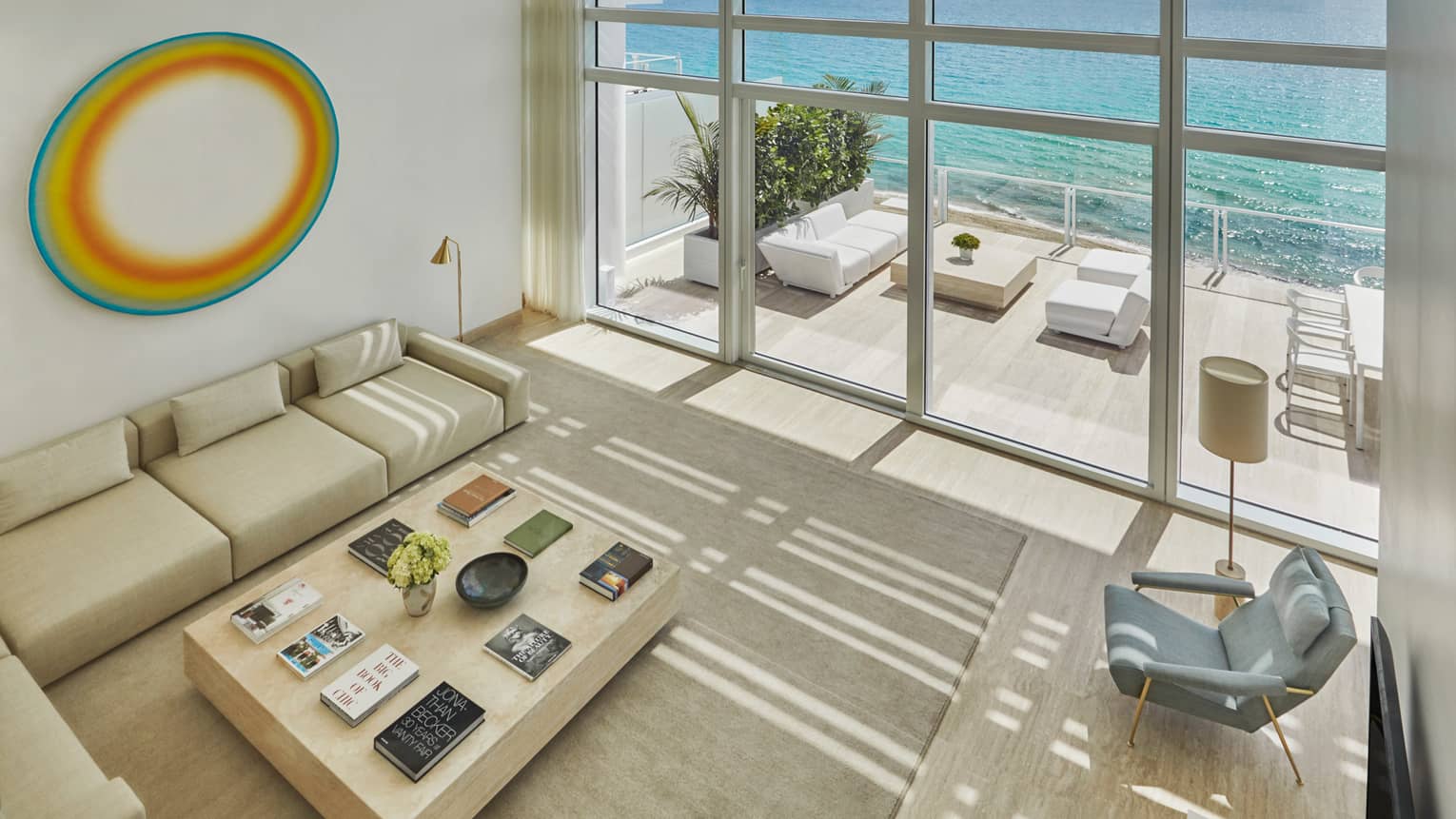 Looking down at bright living room with white L-shaped sofa, armchair, art, glass wall