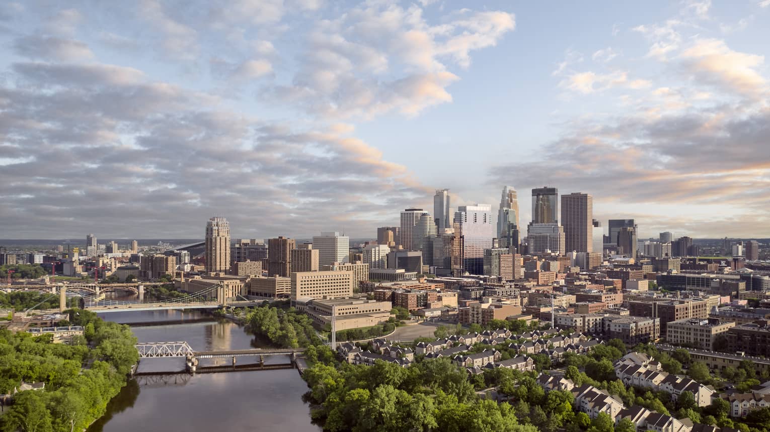 Minneapolis skyline and bridges across Mississippi River, scattered clouds and dense trees