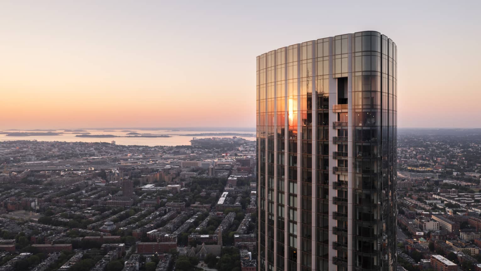 The exterior of a glass and steel skyscraper looking over a city with water in the distance.