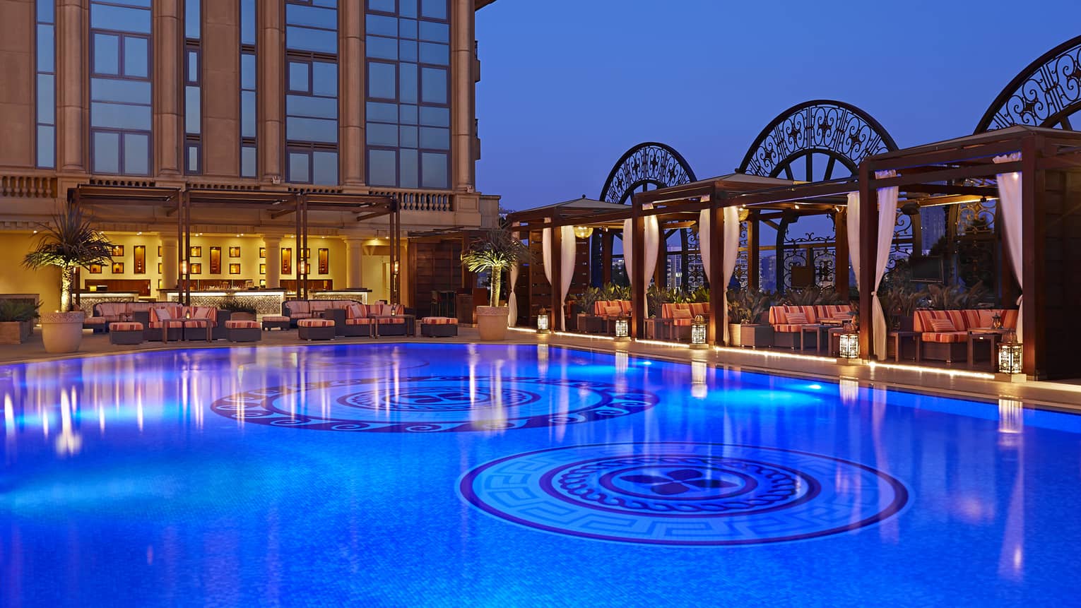 Illuminated blue water in outdoor swimming pool under hotel building at dusk