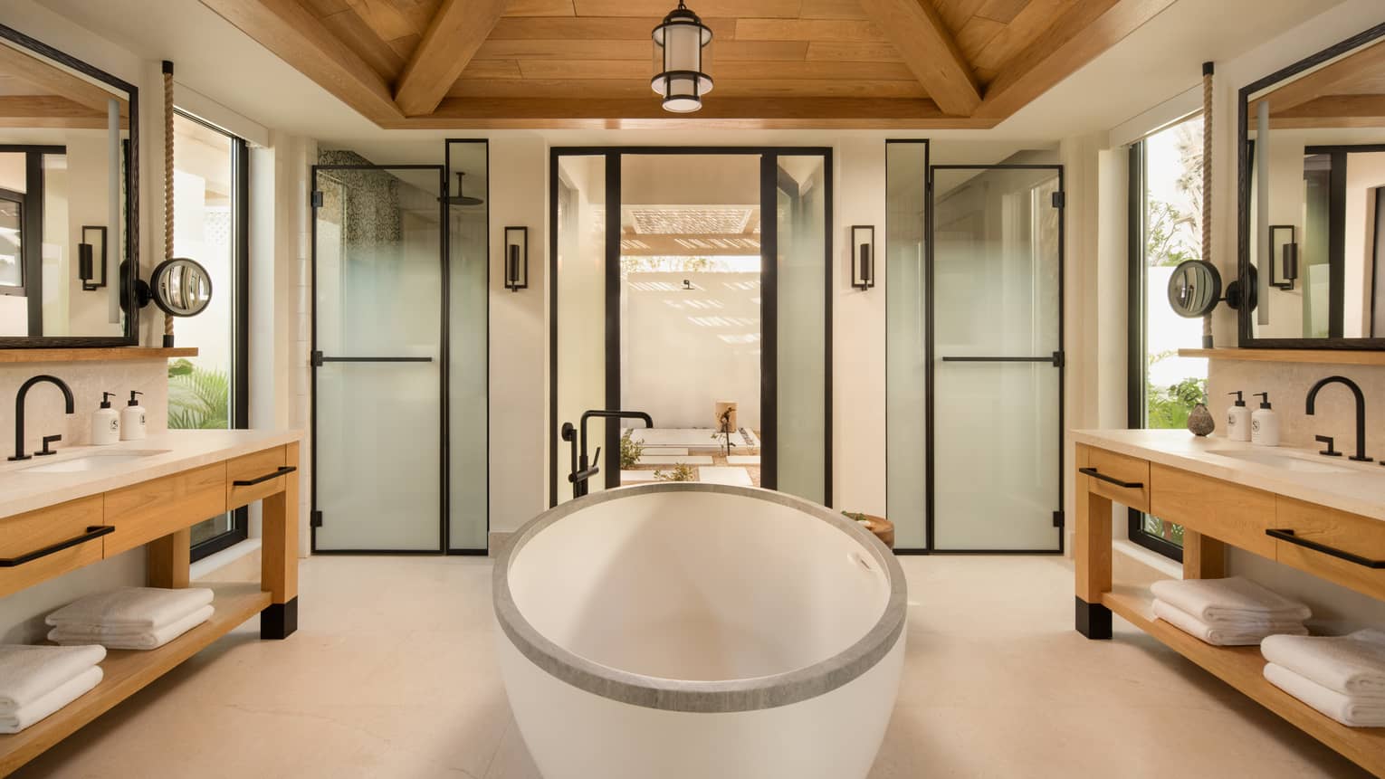 Large luxury bathroom with standalone oval tub in the middle, a vanity on each side, and a vaulted wooden ceiling