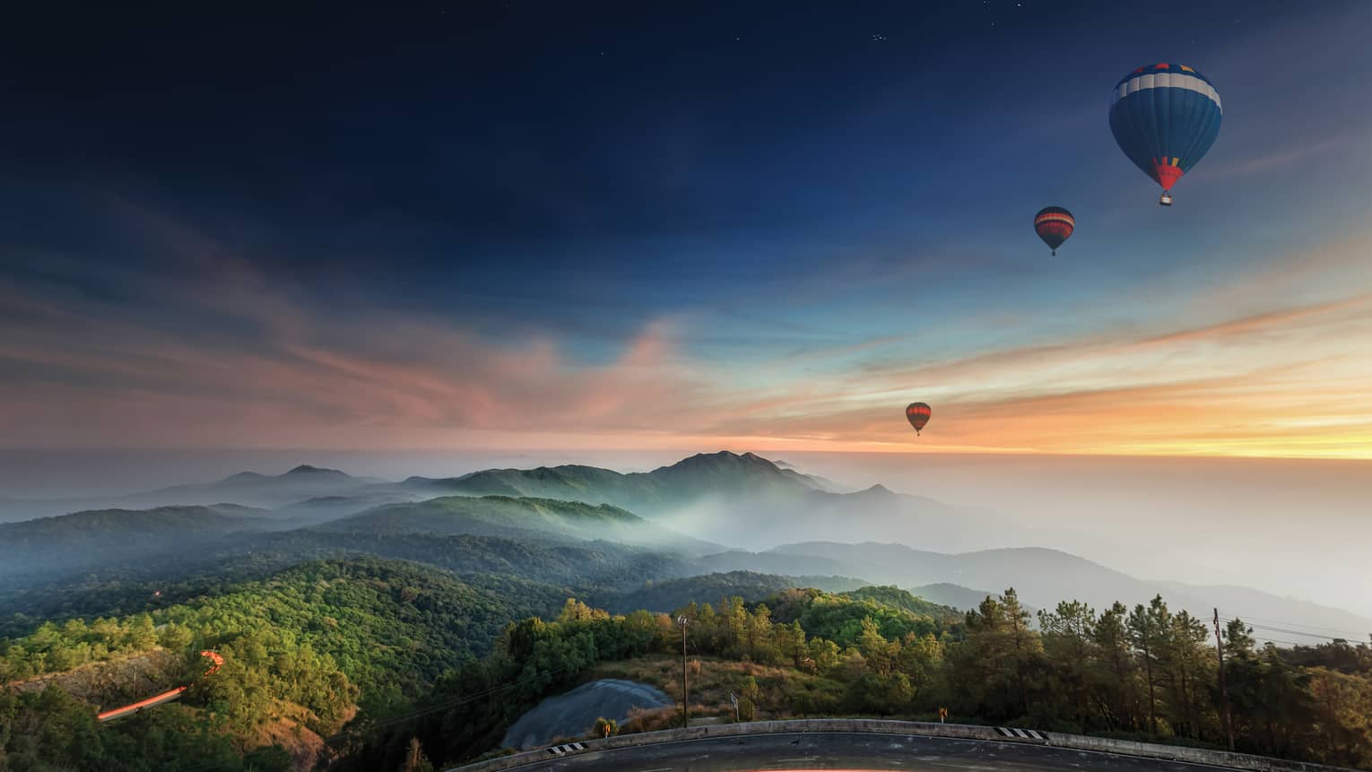 Hot air balloons fly over Chiang Mai at sunrise, mountains in distance 