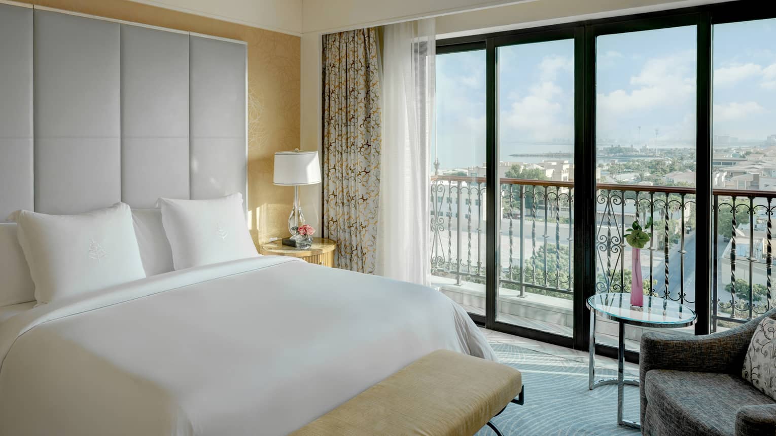 Bedroom with king bed, white sheets, large grey headboard, balcony