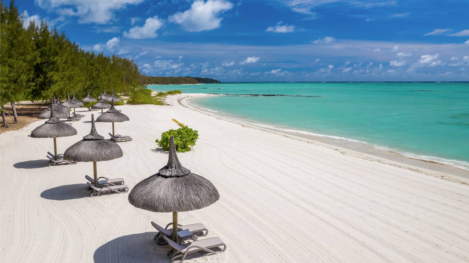 White sand beach with thatched umbrellas and lounge chairs and aqua ocean with blue sky above