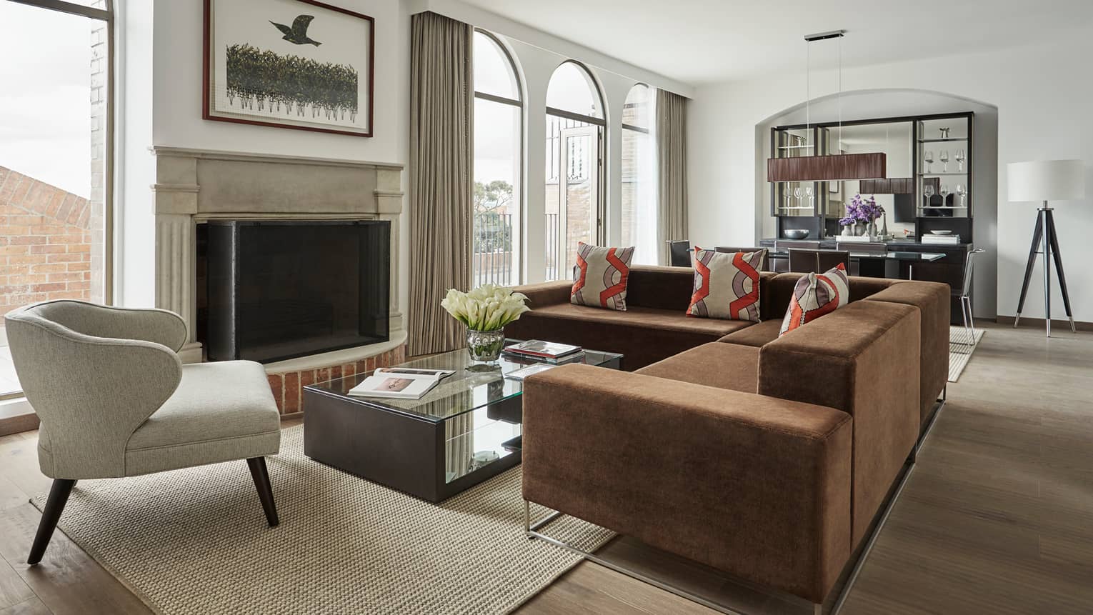 Penthouse Suite living room with L-shaped brown sofa, white armchair, glass coffee table, fireplace