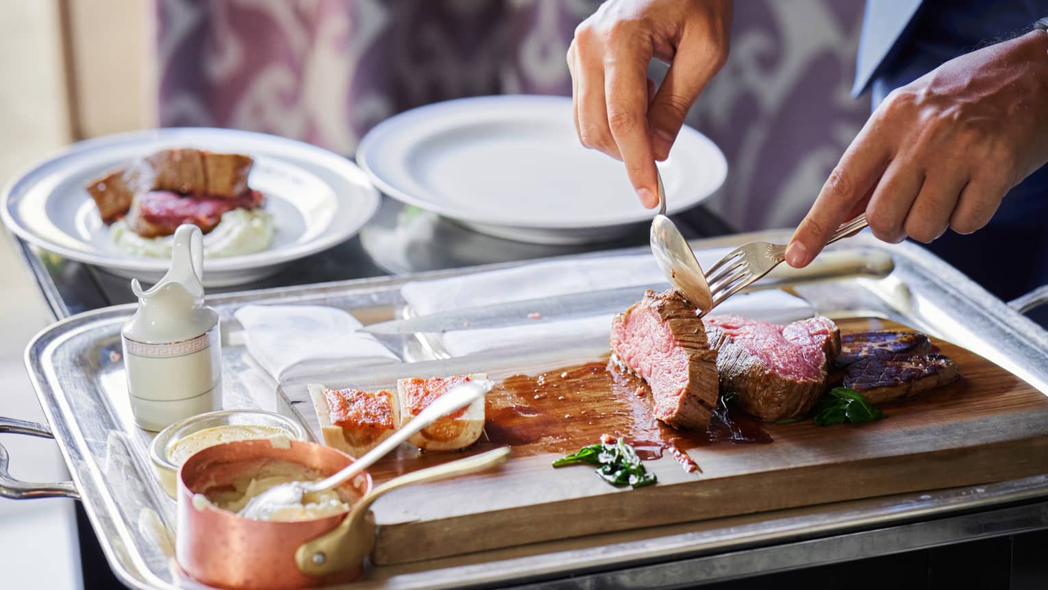Chef carves slices of rare, roasted meat on wood platter