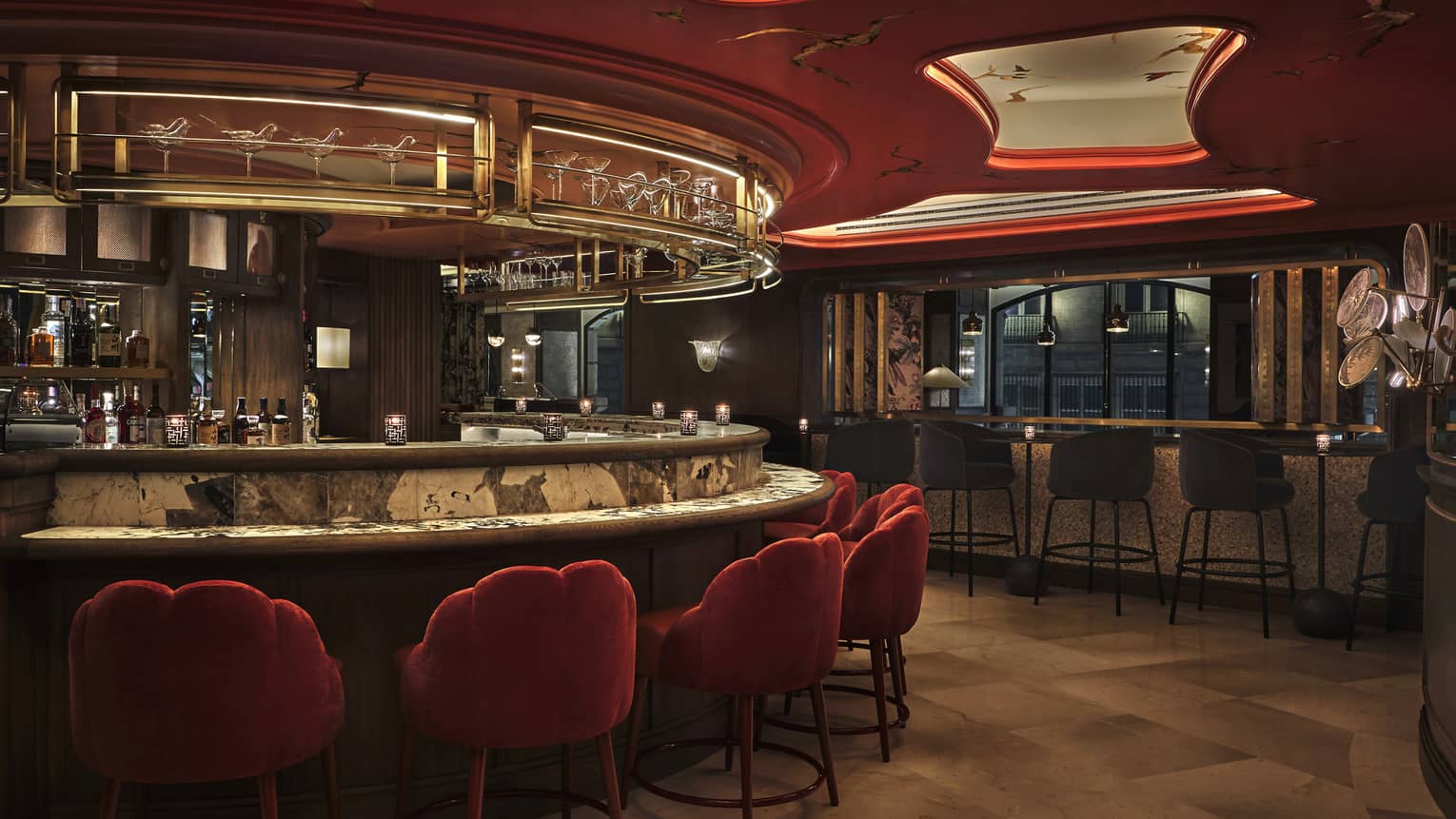Moody bar and lounge with red upholstered chairs, curved bar, red-lit ceiling features