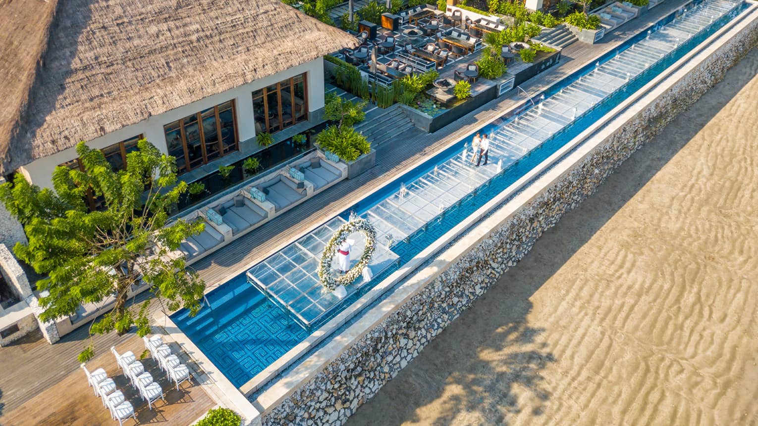 Sundara water wedding, aerial view of two people walking along glass platform over pool