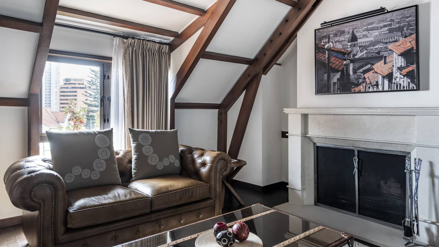 Chocolate leather couch with accent pillows, glass coffee table, fireplace, exposed beam ceilings, glass door to balcony