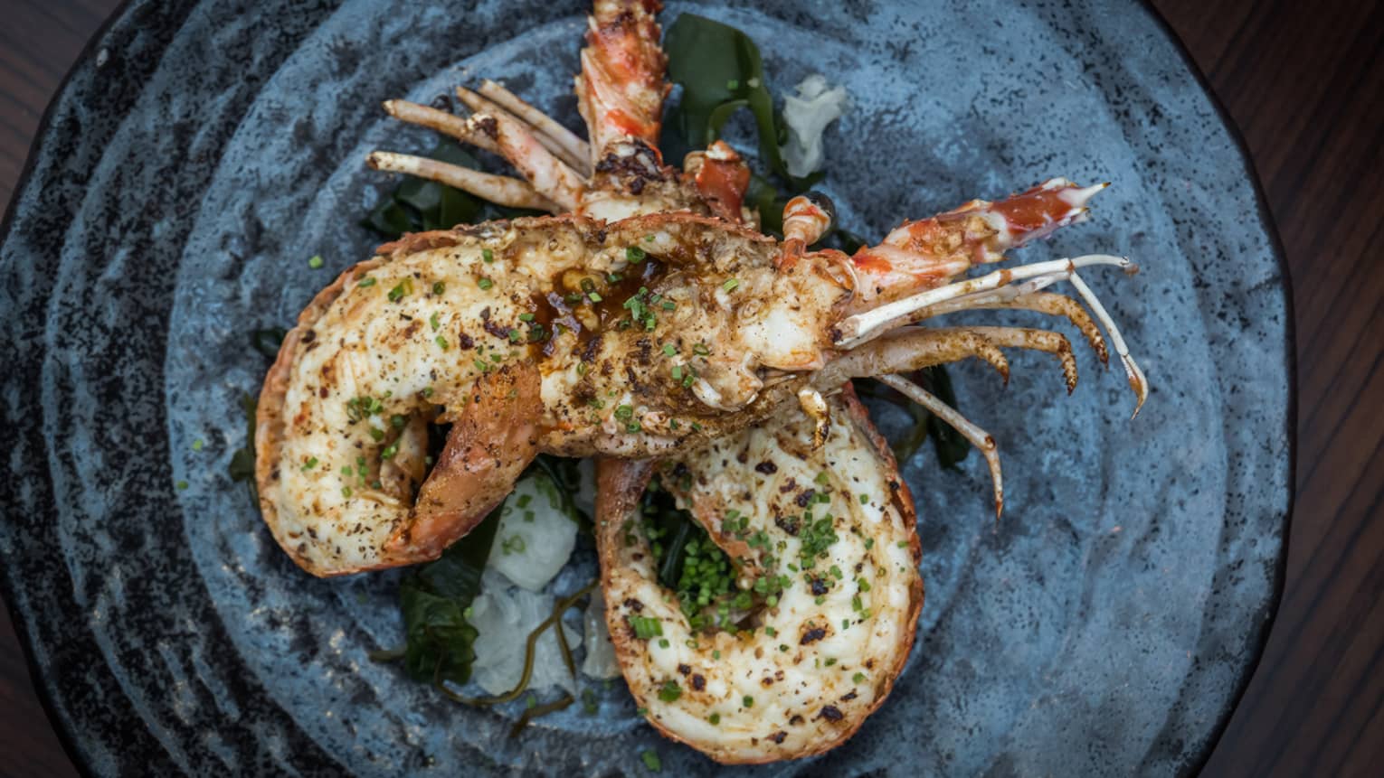 Roasted spiny lobster sprinkled with herbs on stone-like plate