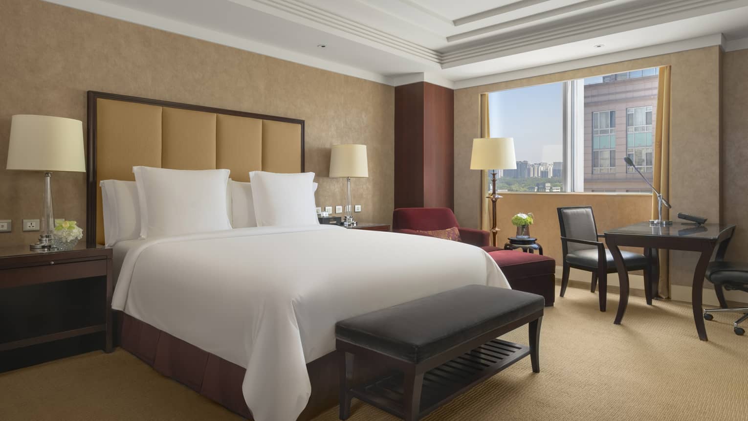 Hotel room with king bed, tan headboard, bench, table and two chairs and window-side chaise