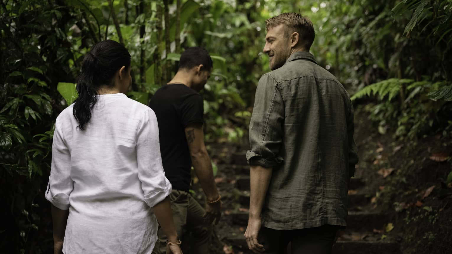 Three people walk along a wooded path with their backs to the camera