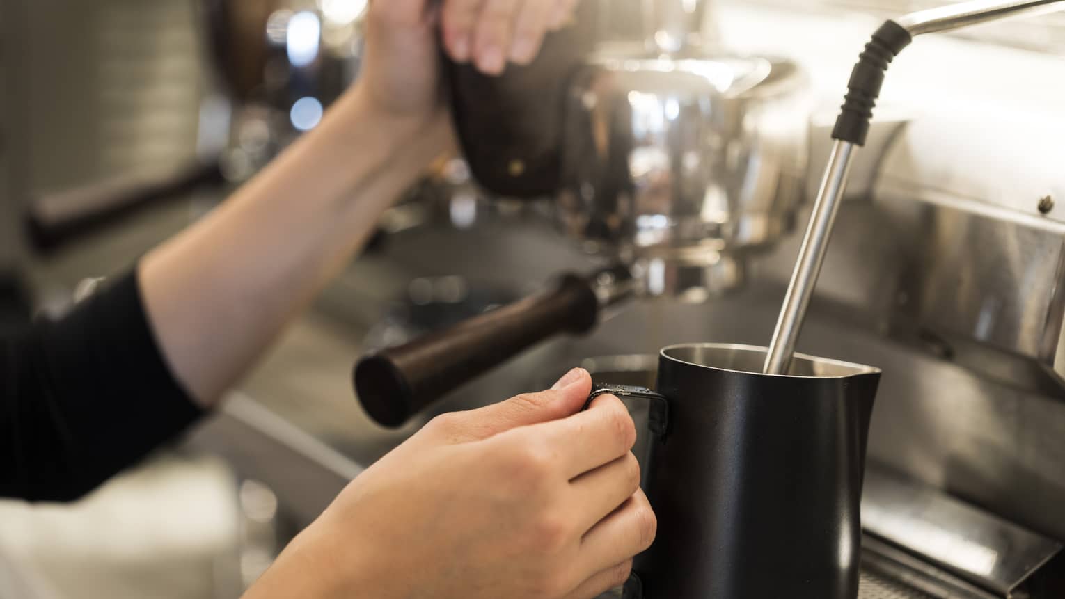 Close-up of hands with milk steamer at espresso machine