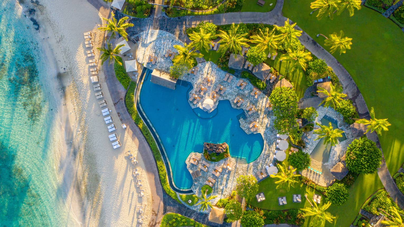 Aerial view of tropical resort pool next to a white-sand beach