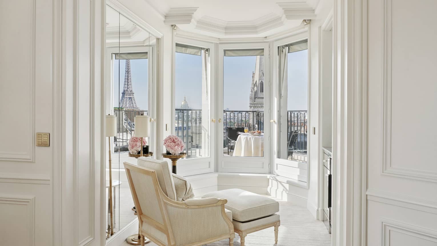 A white room has windows and a balcony with a direct view of the Eiffel Tower