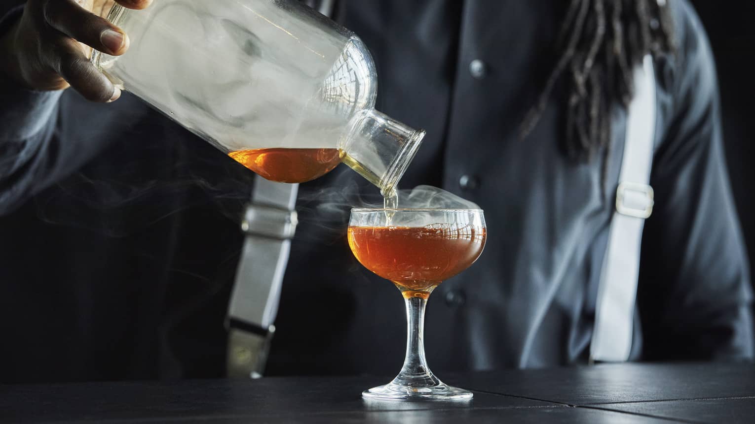 Smoke rolls off the decanter as a Four Seasons staff member pours bourbon into a coupe glass