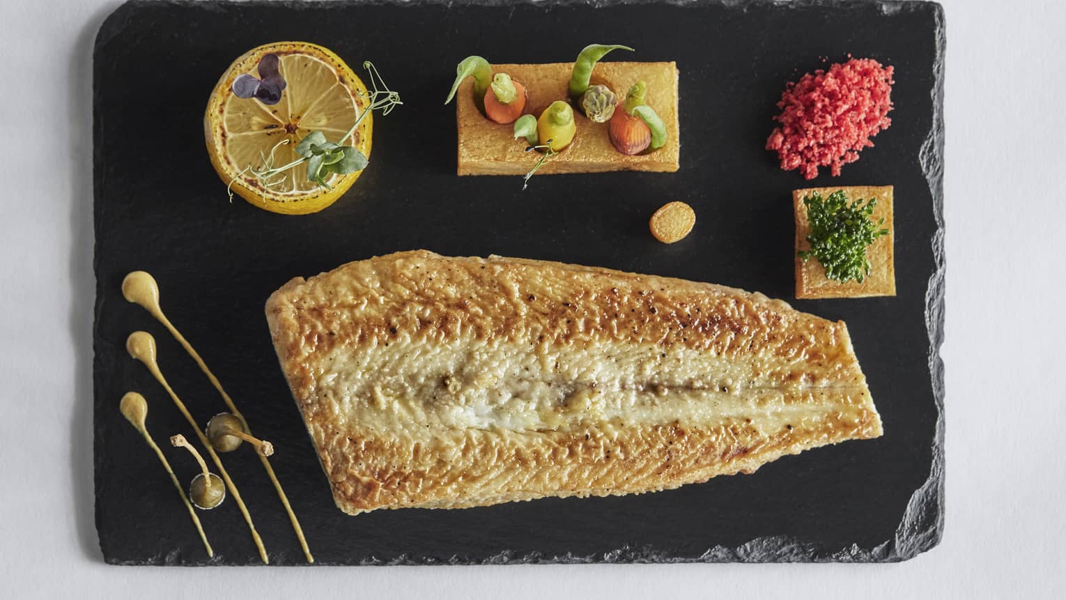 Grilled fish and small vegetables arranged on slate platter