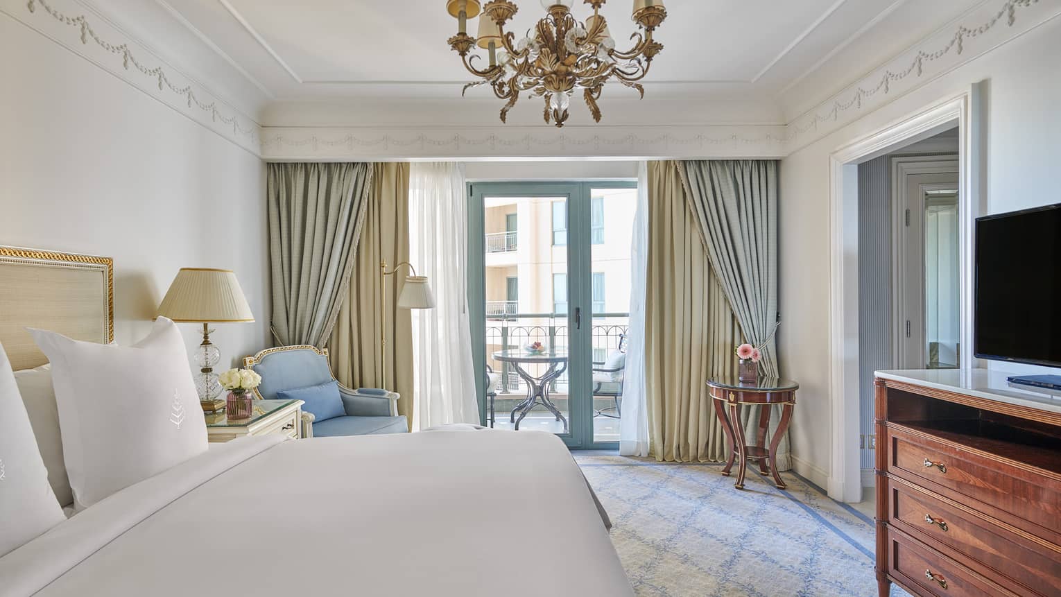 Four Seasons Suite bedroom with king bed, blue corner chaise longue, glass door to veranda, chandelier