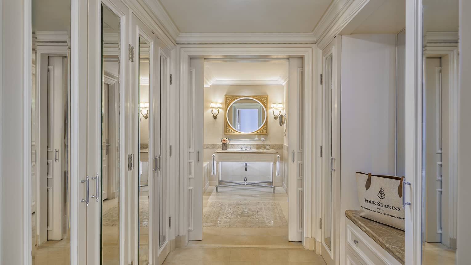 Four Seasons Suite mirrored hallway leading to bathroom with single vanity, lighted wall sconces, oval mirror