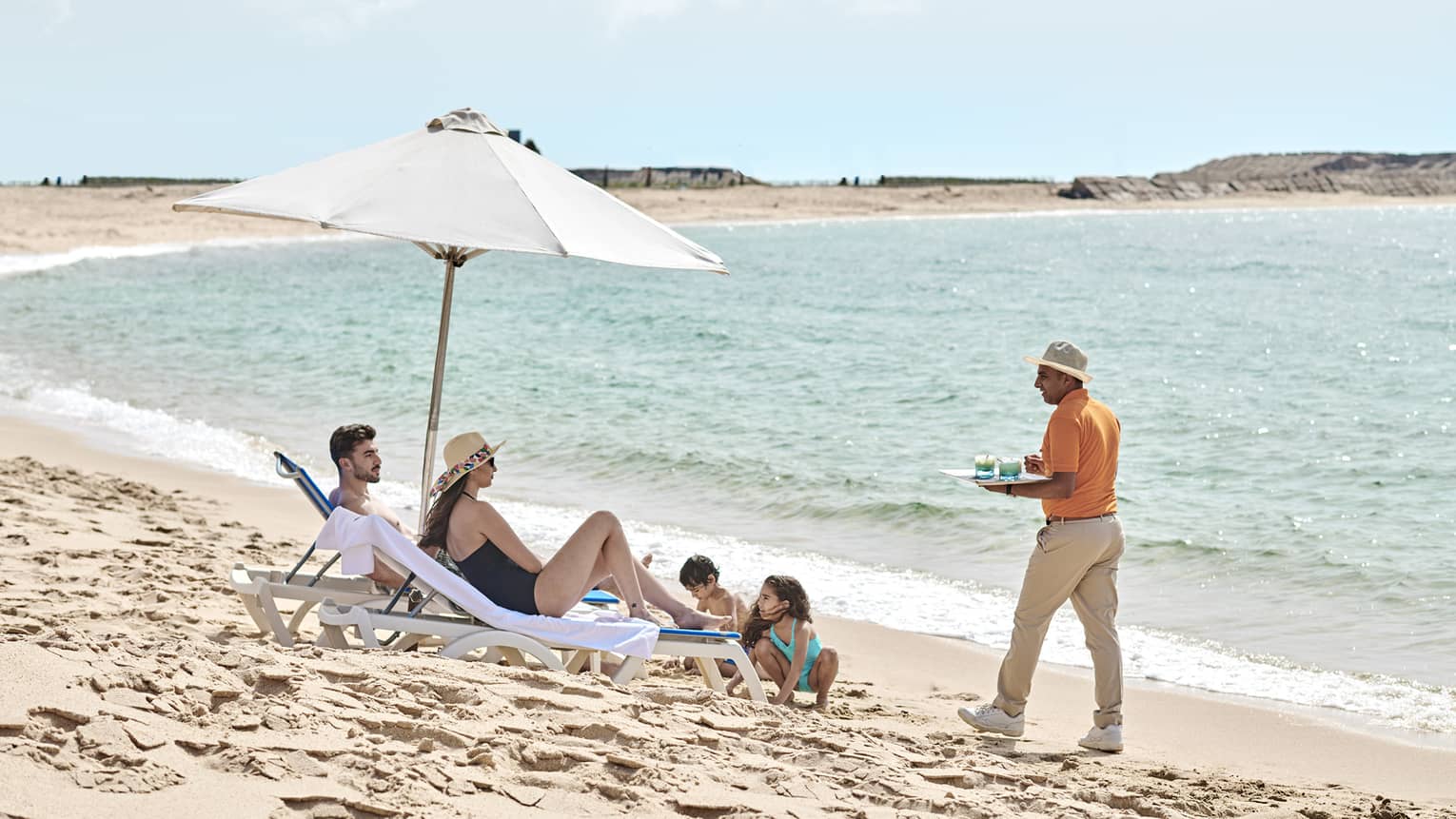 a family lounges on the beach in alexandria while a four seasons staff serves them refreshments