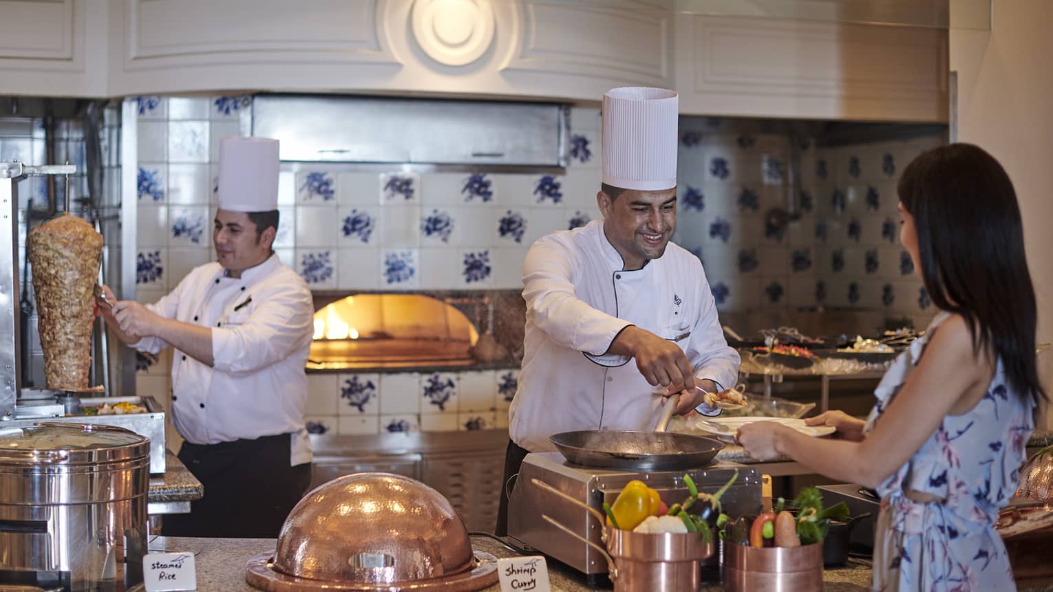 Chef serves woman brunch at Kala Restaurant, another chef slicing meat off a spit in the background