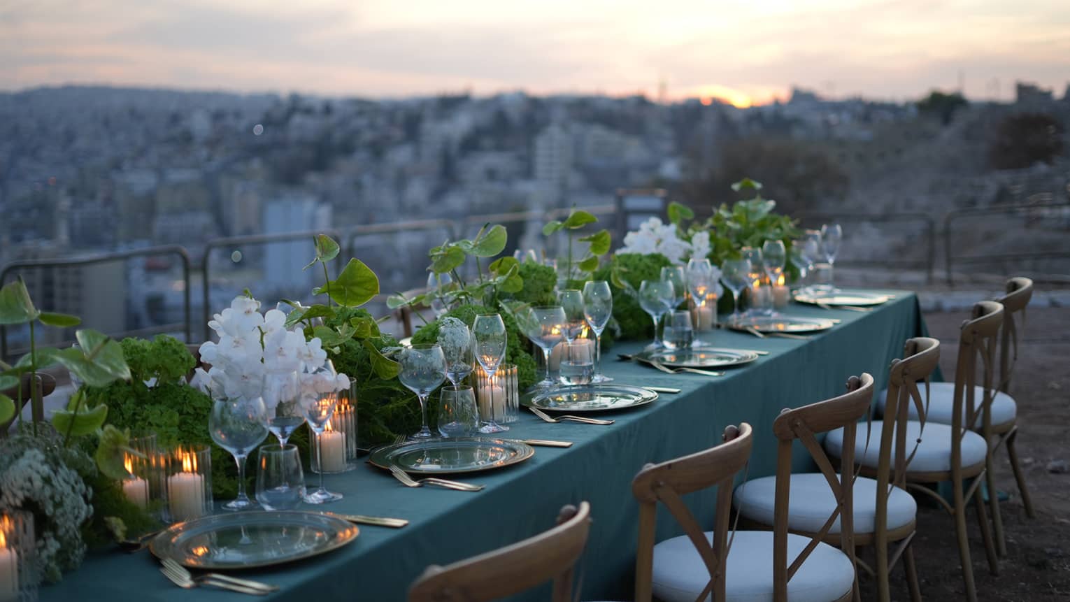 Rectangular table set for a dining event on an open-air terrace overlooking the city below