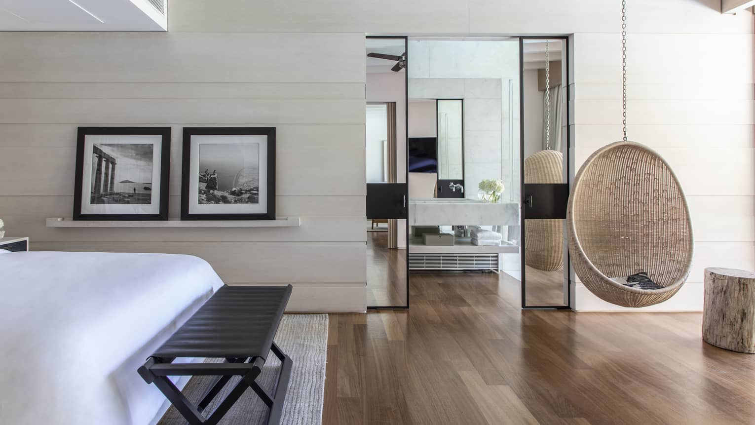 Bedroom with hardwood floors, hanging whicker chair, two framed photos, bench