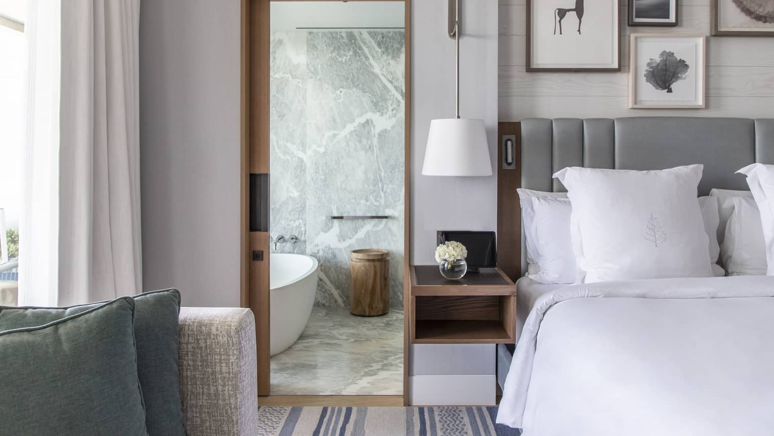 Bed, grey headboard, doorway to marble bathroom with tub