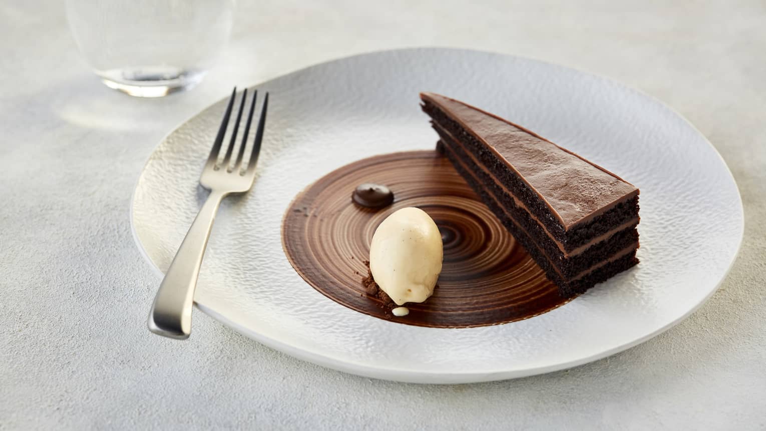 A thin sliced of a layered chocolate ganashe cake garnished with a dallop of cream on a white porcelain plate