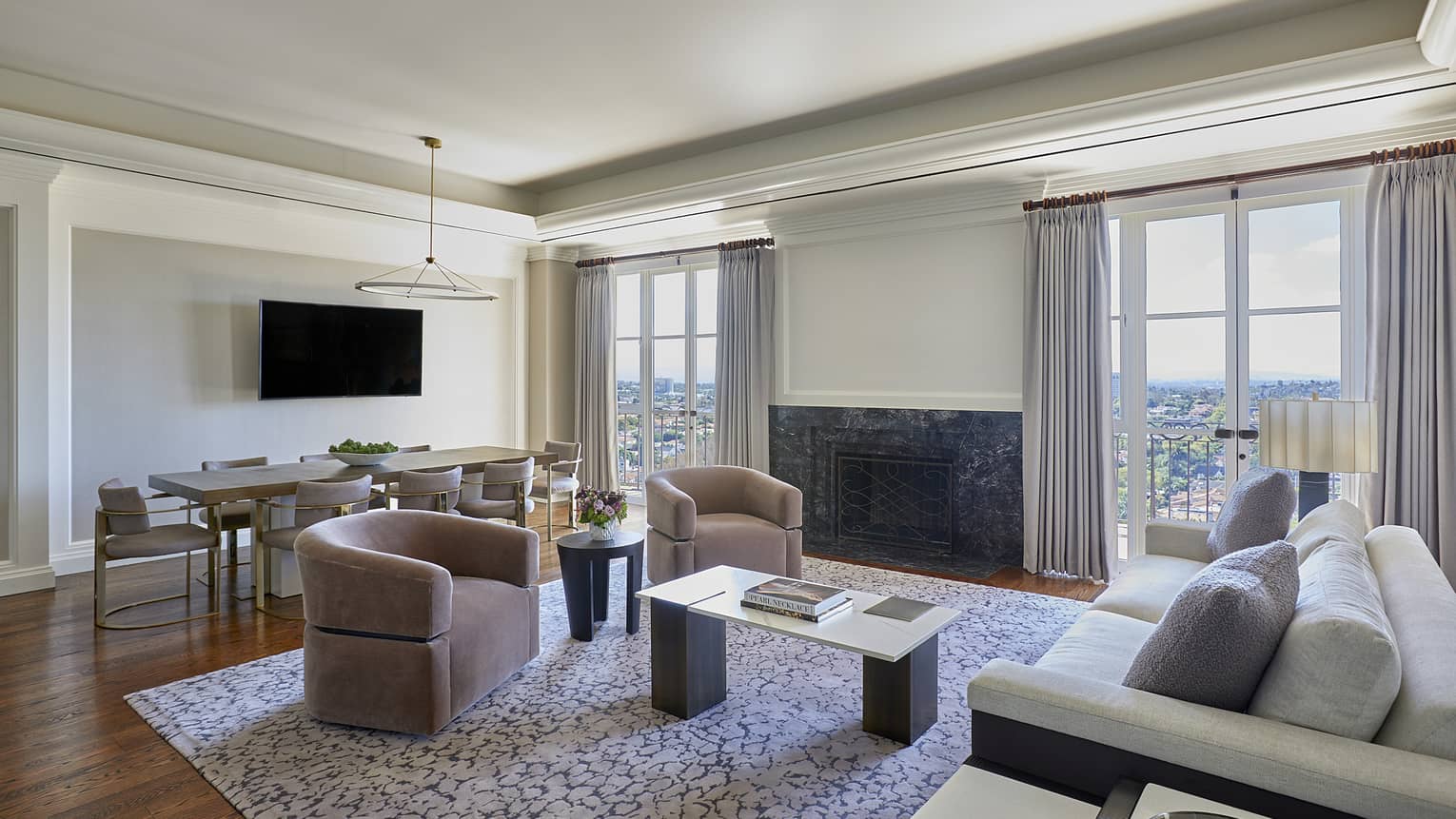 Living room with grey sofa, two mauve-coloured armchairs, dining table, two sets of glass French doors to a balcony
