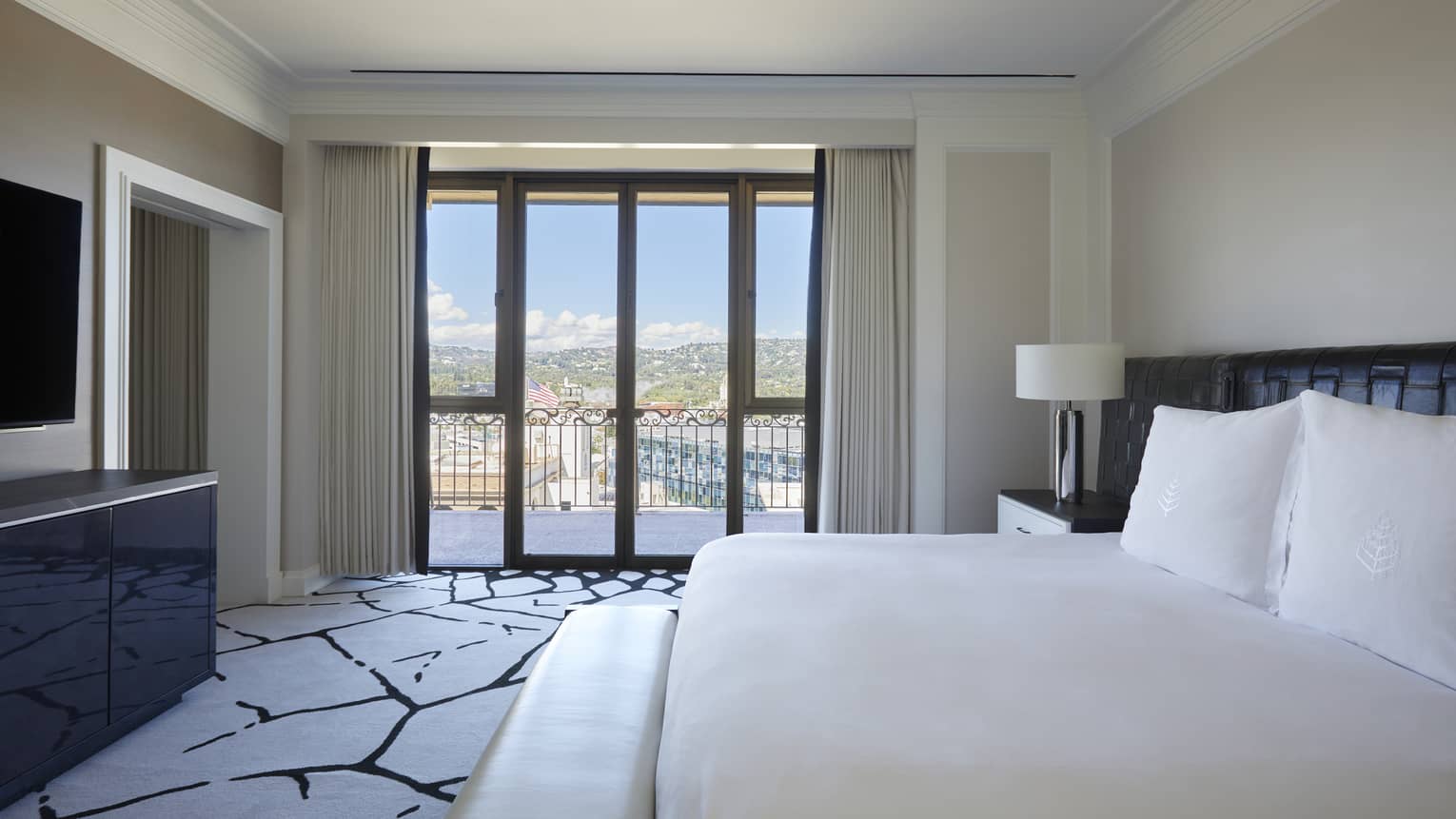 Bedroom with king bed, black and white carpet, black dresser and TV, walk-out balcony