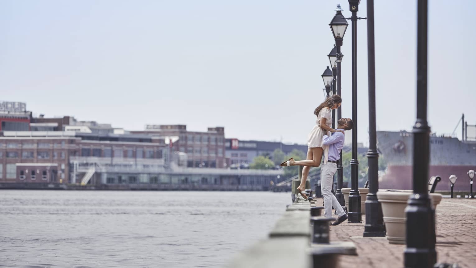 Man holds woman as she stands on ledge of waterfront walkway