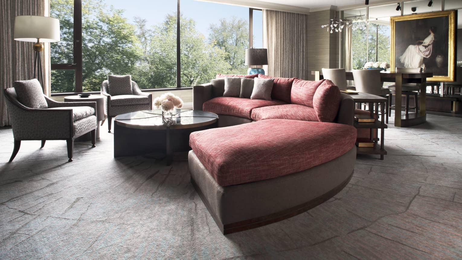 A large circular couch sits at the center of a well lit room, an intricate painting hangs in the background 