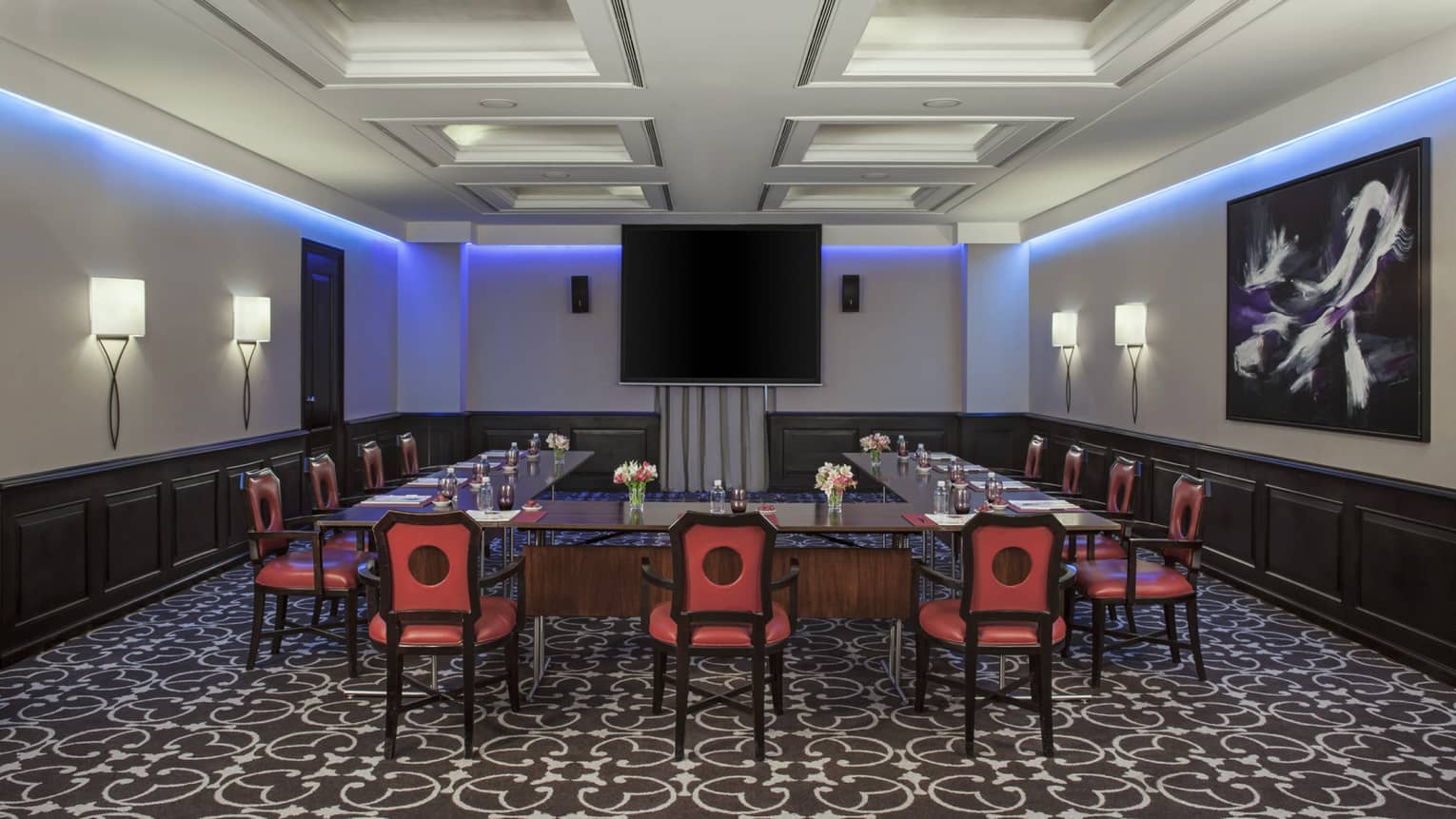 Piero Meeting Room with modular tables and red chairs facing screen, purple accent lighting along ceiling