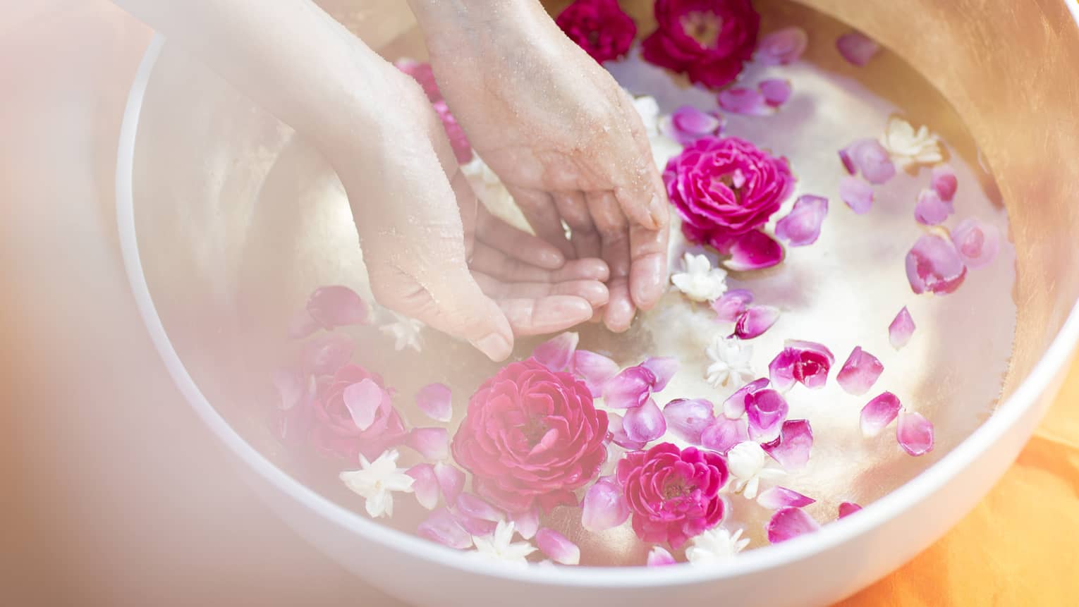 Woman's hands in bowl of water filled with pink and white flowers, petals