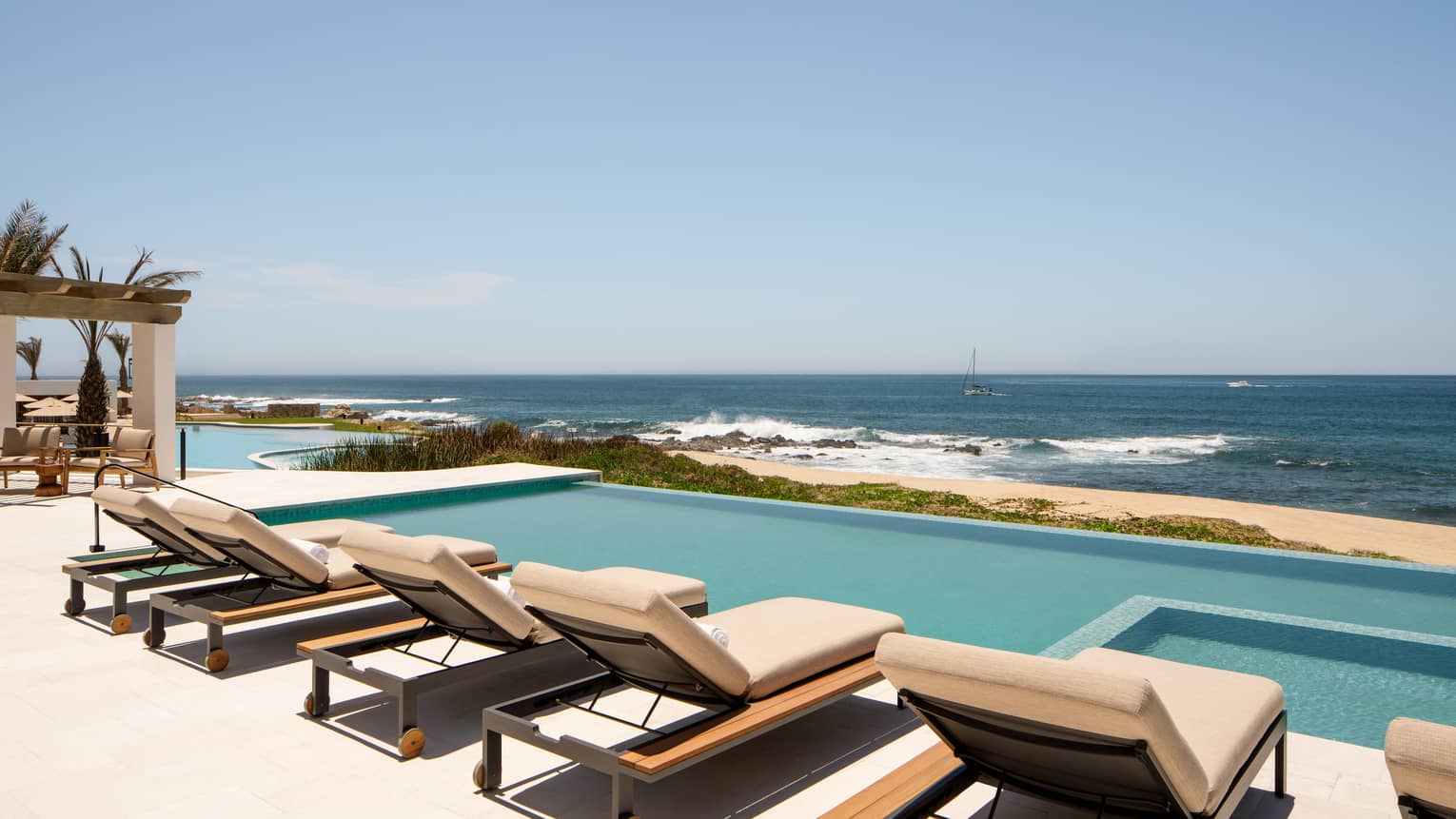 Rectangular pool overlooking the sea and a row of cushioned sun loungers